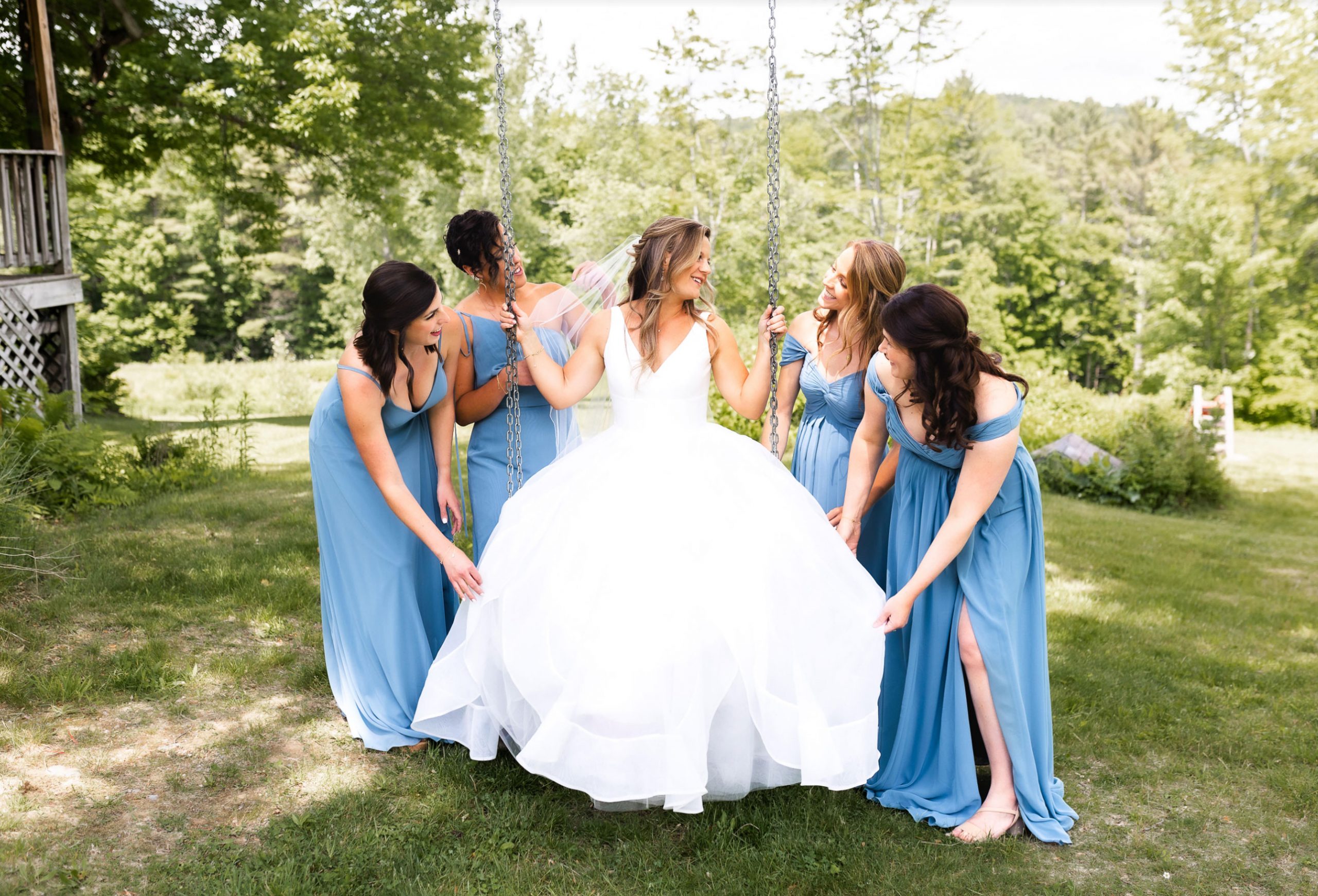 Bride on a swing surrounded by bridesmaids in blue dresses at a Vermont wedding.