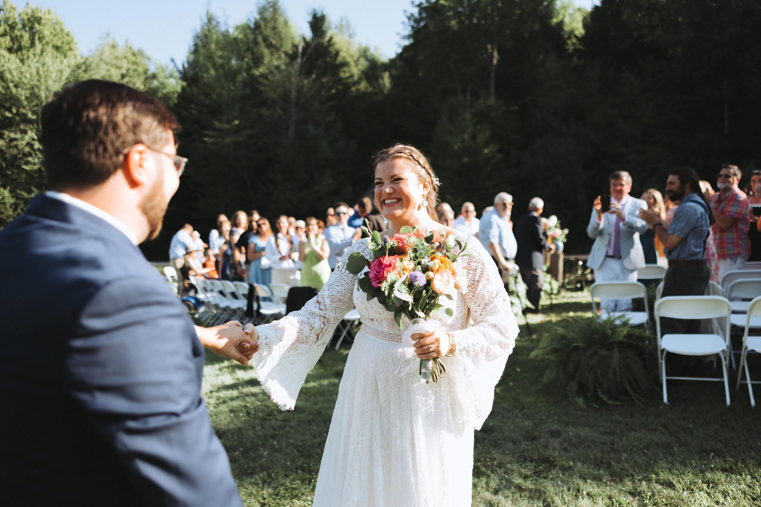Bride and Groom share a moment of joy after their ceremony with their guests clapping behind them.
